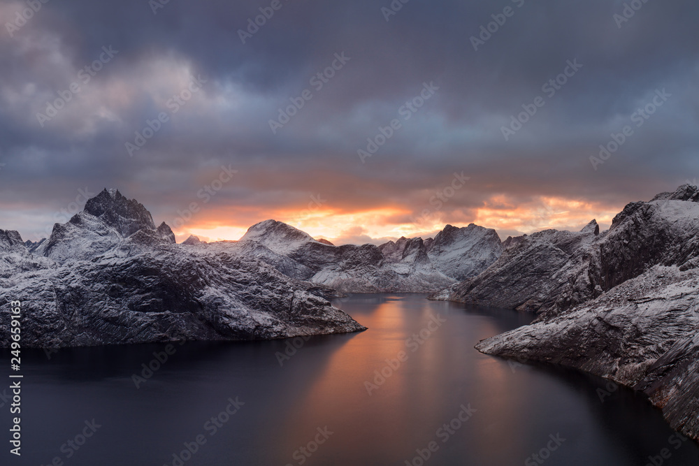 Winter dramatic landscape with snowy mountains, sea, blue and orange cloudy sky reflected in water at sunset. Beautiful Lofoten islands, Norway. Norwegian fjords background. Christmas time concept