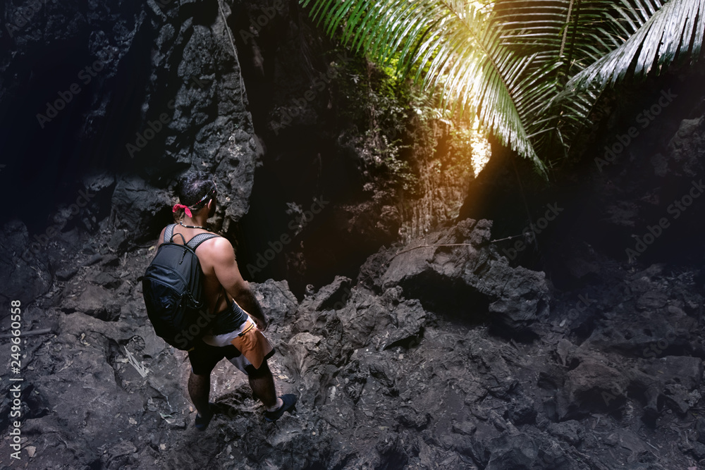 Man climber stands near cave's exit or big rock in darkness