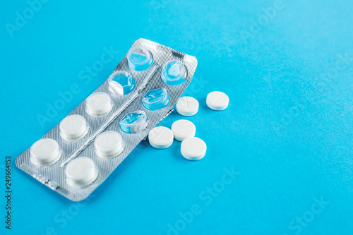 White round pills in pack. Tablets are next to the packaging on a blue background