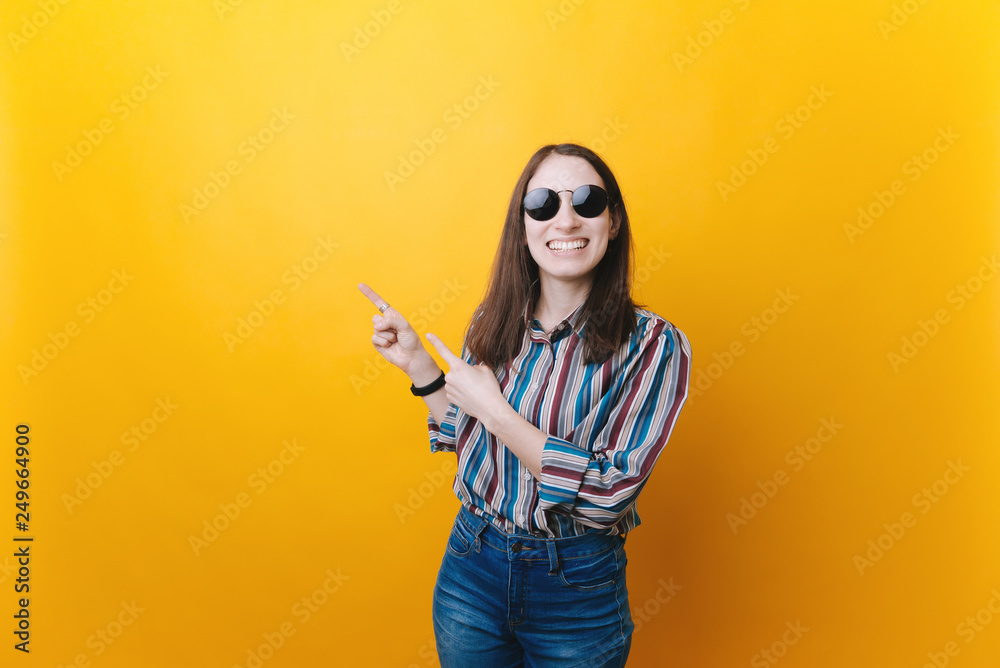 Happy young woman pointing away with both forefingers. Positive lady wearing sunglasses and recommending something. Happy young woman pointing away with both forefingers. Positive lady wearing sunglasses and recommending something.
