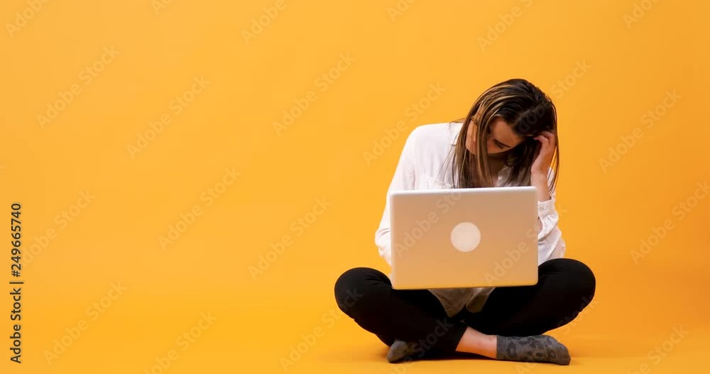 Student girl having an idee while typing on the computer. She is sitting on an yellow background in studio Student girl having an idee while typing on the computer. She is sitting on an yellow background in studio