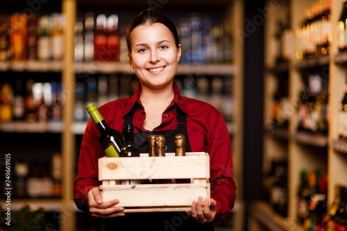 Image of happy woman with wooden box with bottles in her hands in wine shop