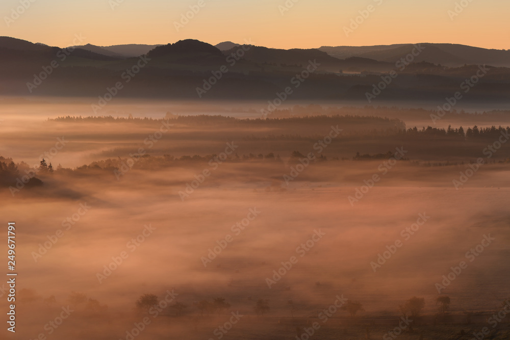 Beautiful summer or autumn sunrise above the forest valley of National park Bohemian Switzerland. Warm sunrise above the deep misty valley. Wonderful landscape background concept. Rays of lights 