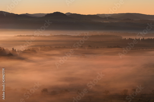 Beautiful summer or autumn sunrise above the forest valley of National park Bohemian Switzerland. Warm sunrise above the deep misty valley. Wonderful landscape background concept. Rays of lights 