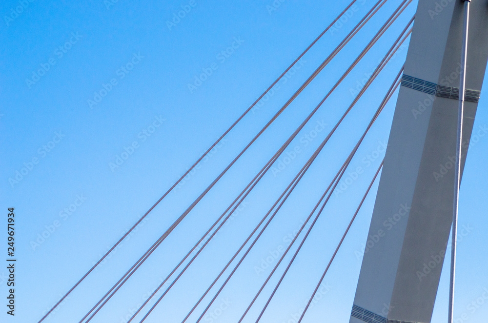 Cable-stayed bridge close-up against the blue sky. White bridge structure on a blue background. Neutral minimalistic background. Cable-stayed bridge close-up against the blue sky. White bridge structure on a blue background. Neutral minimalistic background.