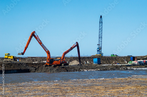 Strengthening the coastline of the river. Two excavators equilibrate the shoreline with a bucket. Construction of the embankment of the pedestrian zone. Russia, the embankment of the Finnish Gulf photo