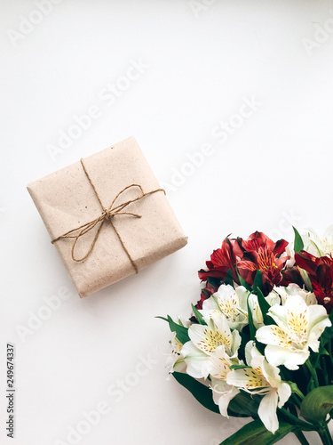 Handmade gift Top view photo Gift box in craft packaging and bouquet of flowers are lying on a white desk