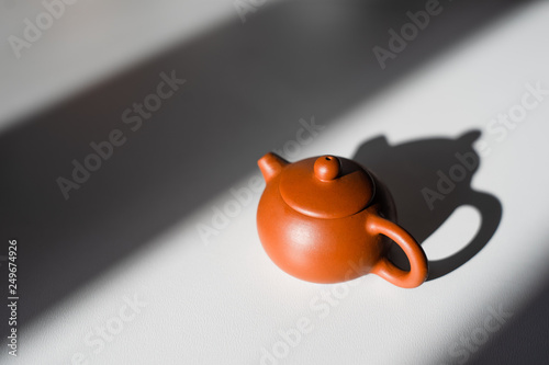little clay teapot standing on the white table in the sunlight between shadow