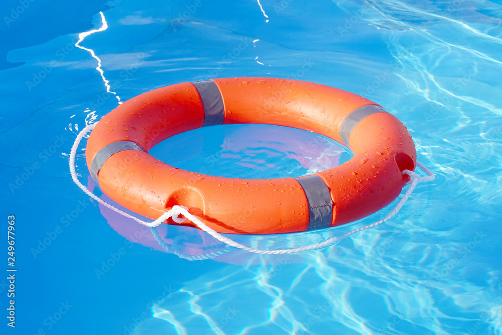 Red lifebuoy pool ring float on blue water. Life ring floating on top of  sunny blue water. Life ring in swimming pool Stock Photo