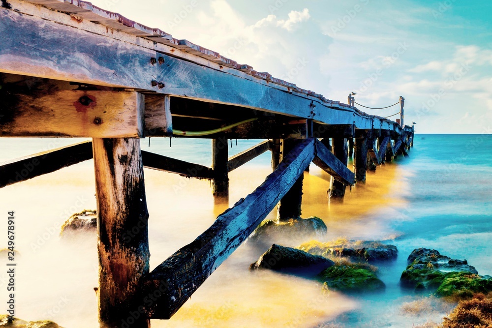 Calm scene of abandoned old rustic wooden jetty out to the sea during a tropical sunny day on the caribbean coast of Mexico