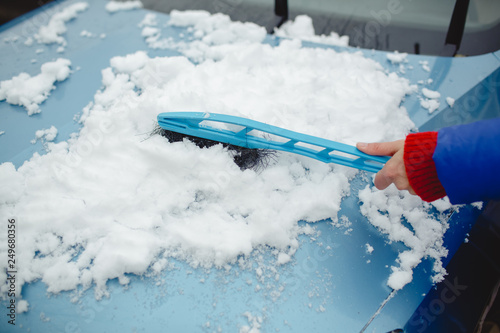 Woman wipes snow machine using winter brush, blue background