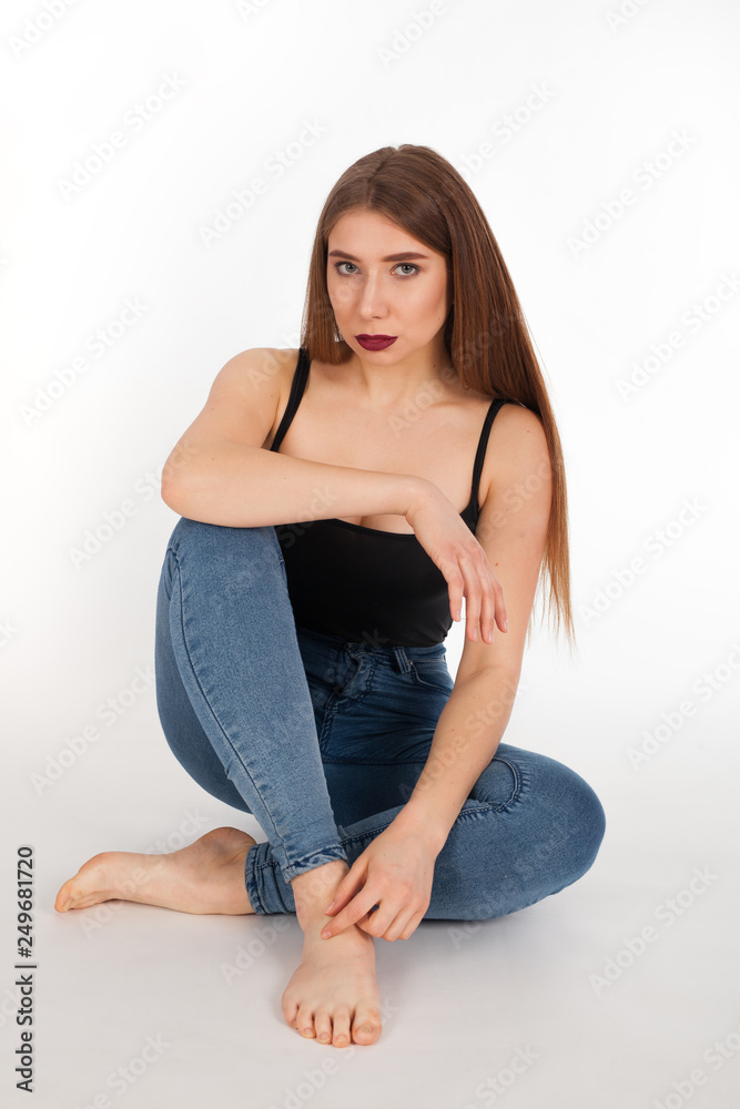 Portrait of a young beautiful girl with make-up isolated on white background. A woman in jeans and a t-shirt is sitting and looking at the camera. Portrait of a young beautiful girl with make-up isolated on white background. A woman in jeans and a t-shirt is sitting and looking at the camera.