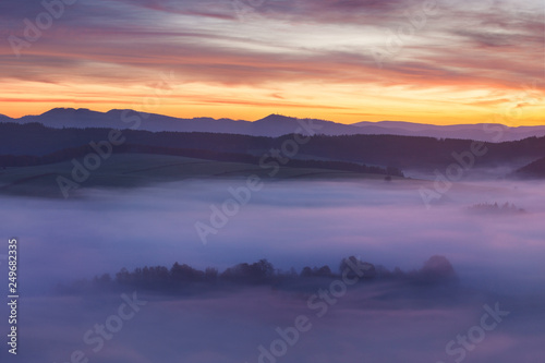 Sunset Over Misty Landscape Scenic View Of Foggy Morning Sky With Rising Sun Above dreamy Forest. Mountain range with visible silhouettes through the morning colorful fog  Beautiful background concept © Michal