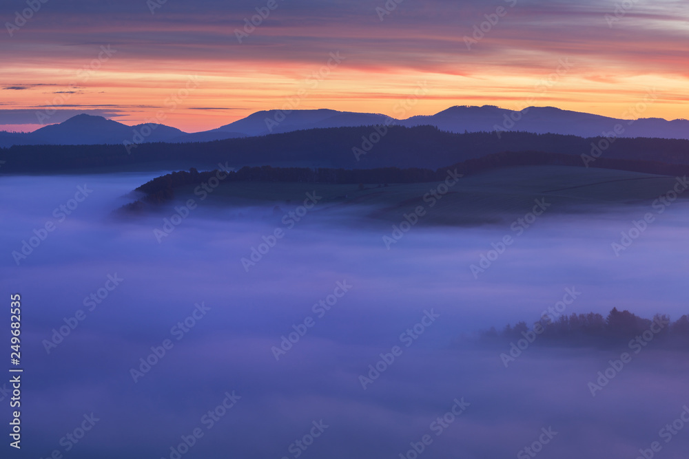 Sunset Over Misty Landscape Scenic View Of Foggy Morning Sky With Rising Sun Above dreamy Forest. Mountain range with visible silhouettes through the morning colorful fog  Beautiful background concept