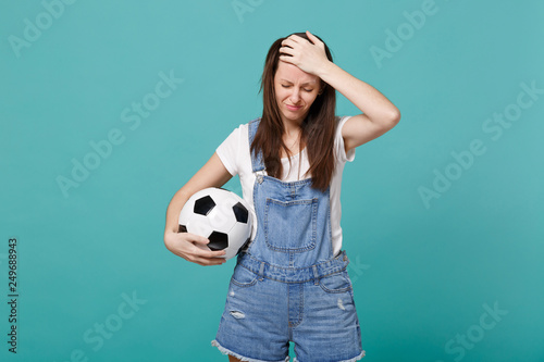 Distempered woman football fan support favorite team with soccer ball putting hand on forehead isolated on blue turquoise background. People emotions, sport family leisure concept. Mock up copy space. © ViDi Studio