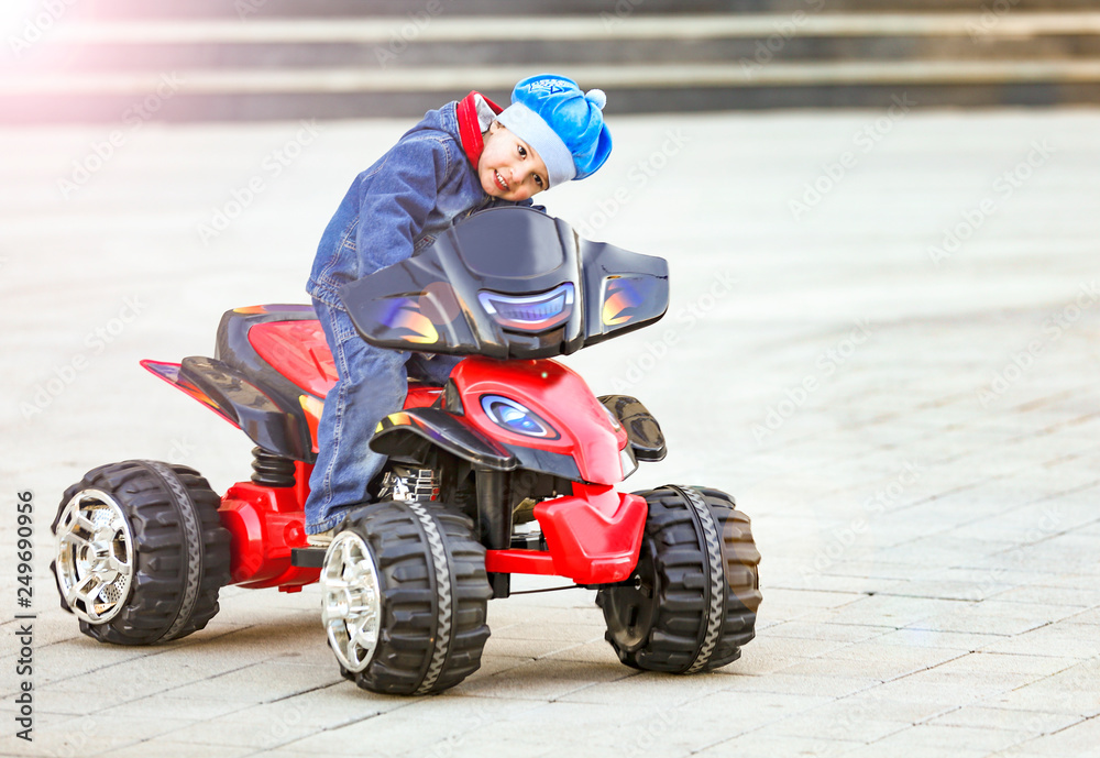 Funny little boy rides an electric red car in the city park Funny little boy rides an electric red car in the city park