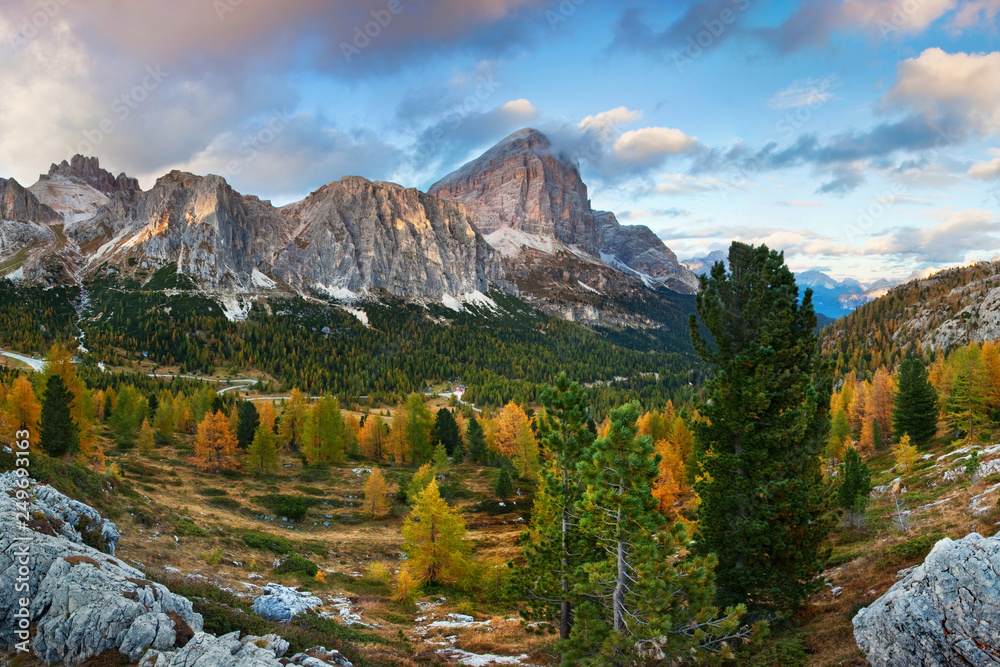 Gorgeous sunny view of Dolomite Alps with yellow larch trees. Colorful autumn scene of Tofana di Mezzo mountain range. Passo Falzarego location, Italy, Europe. Beauty of nature concept background.