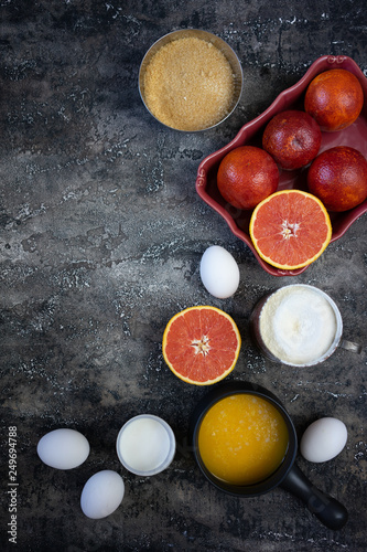 Set of ingredients to bake a blood orange cake. Cooking from a recipe. Top view. Blood oranges, eggs, sugar, milk, butter on a textured black background