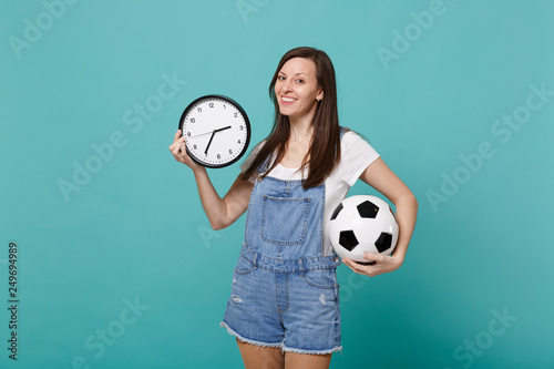 Attractive young woman football fan cheer up, support favorite team with soccer ball, round clock isolated on blue turquoise wall background. People emotions, sport family leisure lifestyle concept.