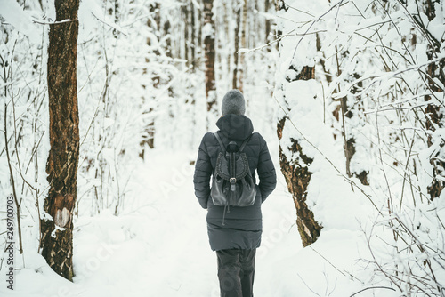 a back shot of a Beautiful youngwoman dressed in a black winter jacket with leather backpack walks in the snowy forest wood .landscape background behind © skrotov