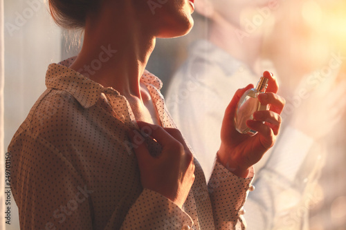 Quadro em tela Stylish woman in blouse spraying a bottle of favorite perfume at sunset