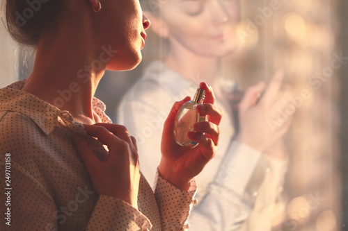 Stylish woman in blouse spraying a bottle of favorite perfume at sunset. Fashion, beauty and style photo