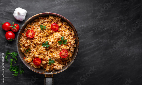 Homemade delicious pilaf with chicken, fresh parsley and ripe vegetables in a pan for lunch on a dark background. Top view