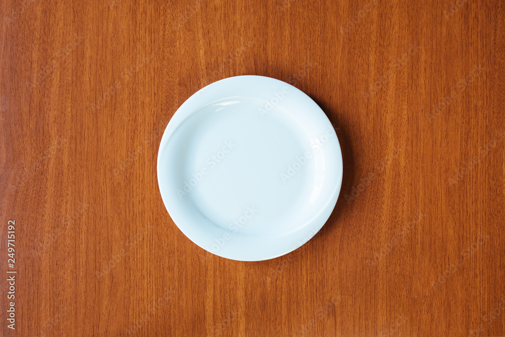 Empty white plate on wooden table from top view Empty white plate on wooden table from top view