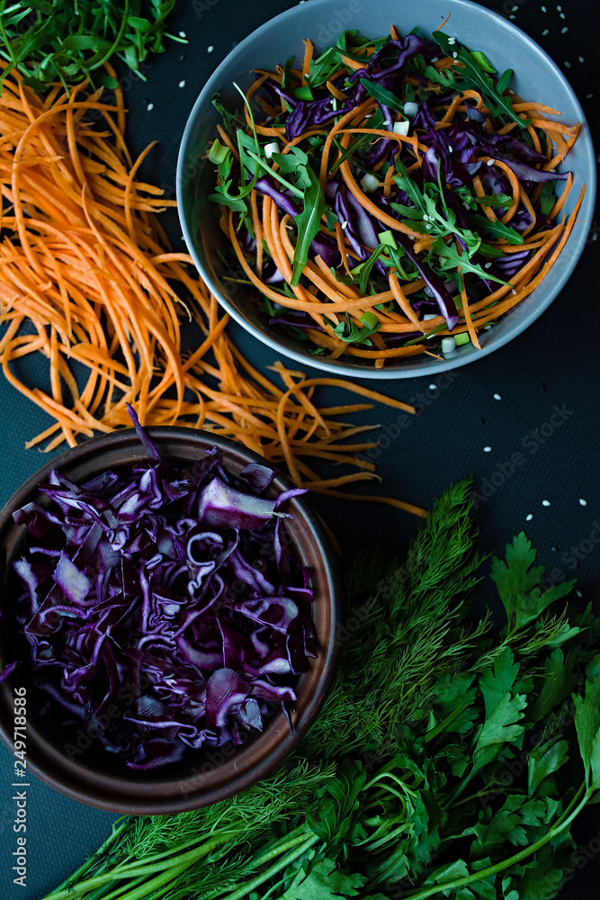 Salad of red cabbage, carrots and greens. Decorated with sliced vegetables and herbs. Cutting strips. Dark background. View from above.
