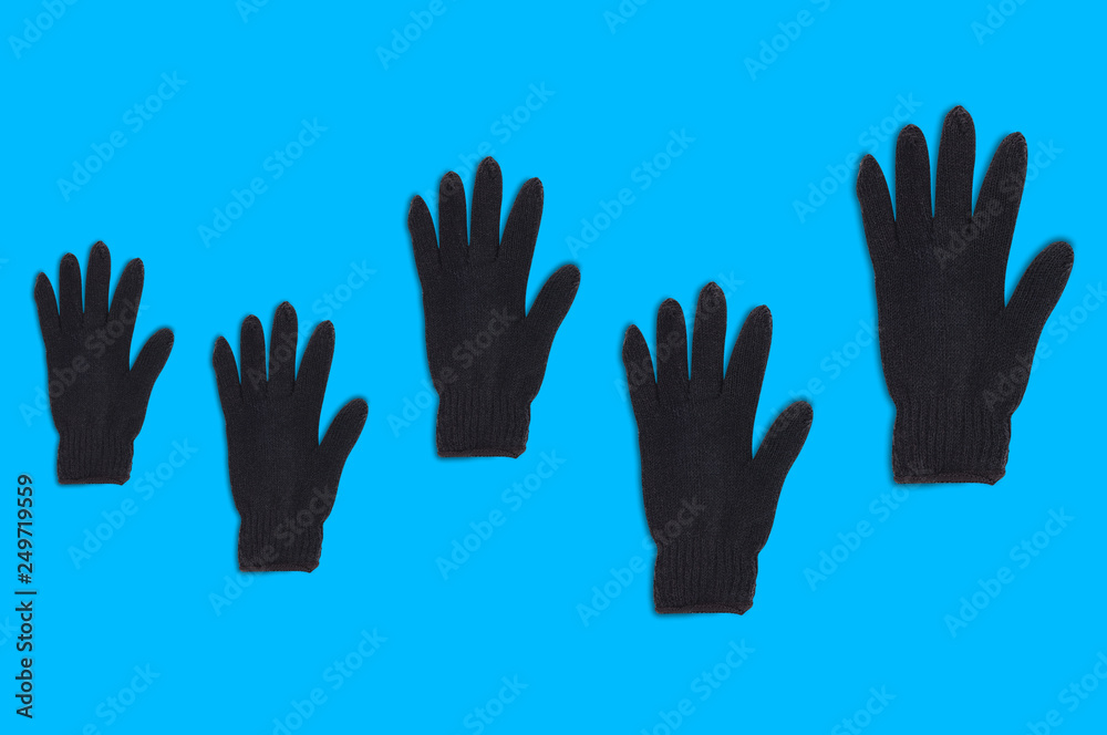 Fototapeta premium Horizontal row of black warm woolen gloves from small to large on blue background. Top view