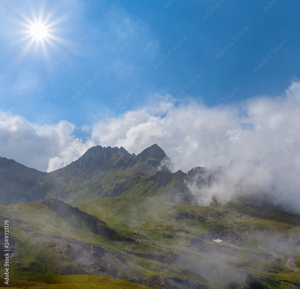 majestic mountain ridge in a dense clouds under a sparkle sun