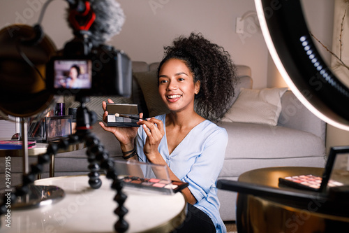 Smiling woman holding a makeup palette while recording her video for blog photo