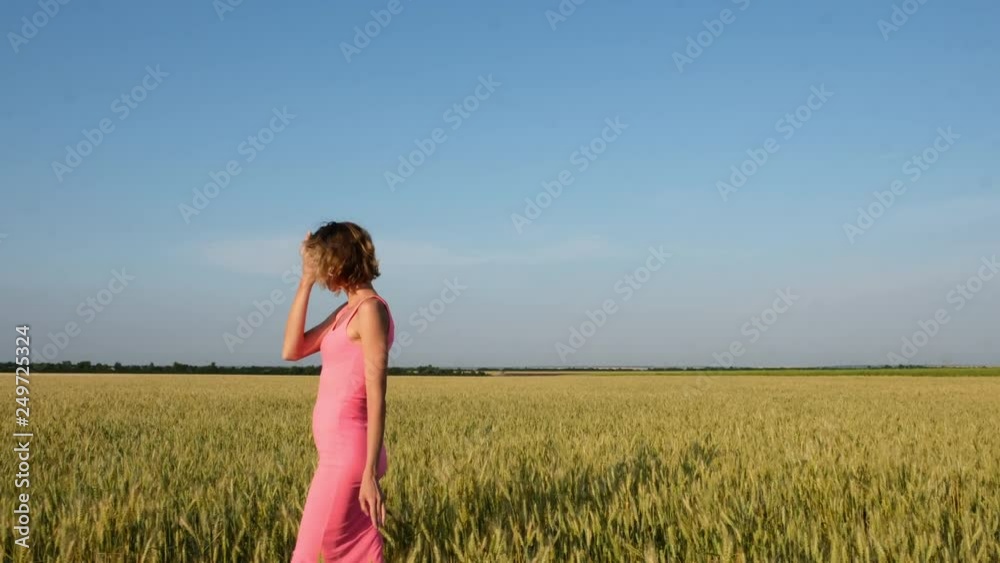 Young woman in a dress walking through the wheat field at sunset. Side view Young woman in a dress walking through the wheat field at sunset. Side view