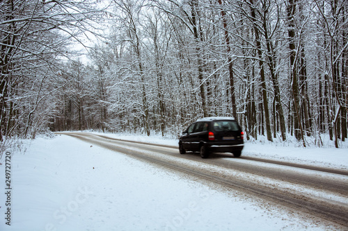 Black car driving through the woods on an asphalt road covered with snow