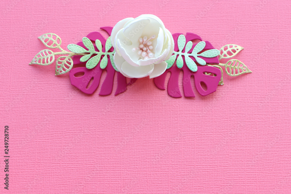 white handmade flower and paper leaves on a pink paper textural background. copy space.. white handmade flower and paper leaves on a pink paper textural background. copy space..
