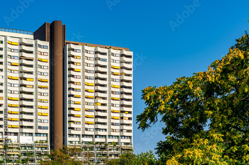 White residential building with green plants on the balconies and yellow awnings