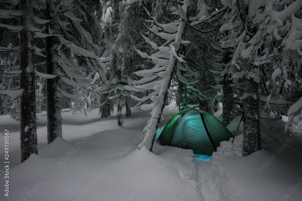 Night shot, long exposure, sleeping in the snow outside. Night bivouac in the mountains, millions of hours under the night sky, green lighted tent in the Alps.