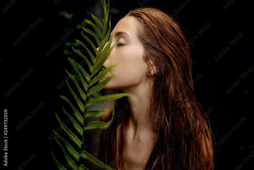 beautiful woman with red hair posing with a fern leaf on dark background beautiful woman with red hair posing with a fern leaf on dark background
