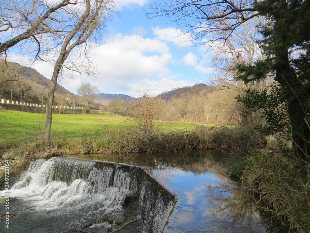 waterfall in a flowing stream with a view of a village and a blue sky waterfall in a flowing stream with a view of a village and a blue sky