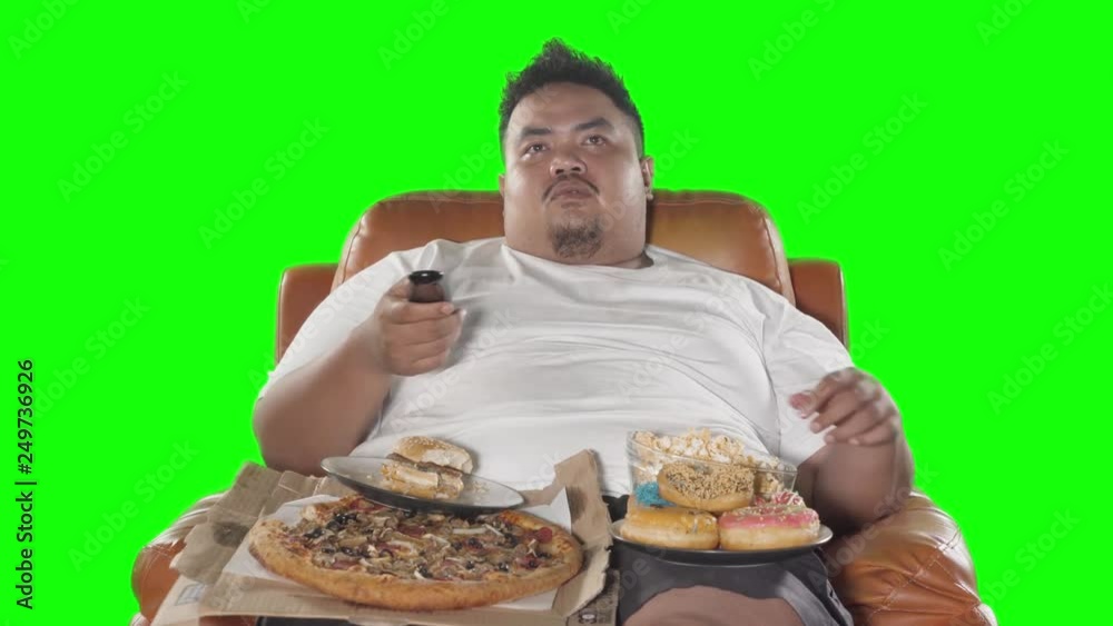 Obese man watching TV while eating junk foods like pizza, donuts, and popcorn on the sofa. Shot in 4k resolution with green screen background Obese man watching TV while eating junk foods like pizza, donuts, and popcorn on the sofa. Shot in 4k resolution with green screen background