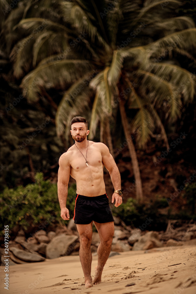 sexy handsome sportsman walking on the beach with palm trees in Thailand sexy handsome sportsman walking on the beach with palm trees in Thailand