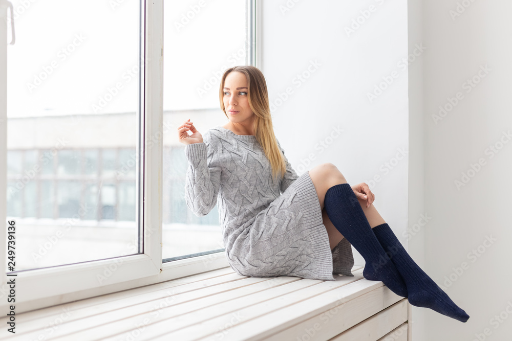 People and fashion concept - Beautiful dreaming woman in knitted dress sitting on a sill