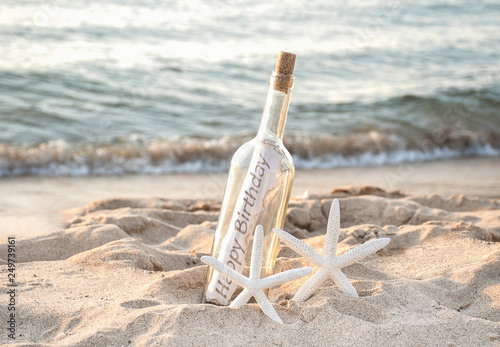 pair of white starfish with happy birthday message in a bottle on beach sand