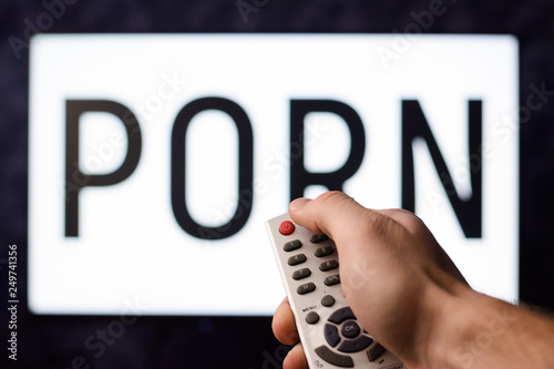 Young man having watched a ponography film pushes red power button on a remote controller of a TV set to turn off a TV set photo