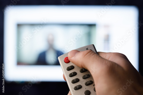 Irritated young man pushes red button on a remote controller in order to turn off a smart TV set with video in browser