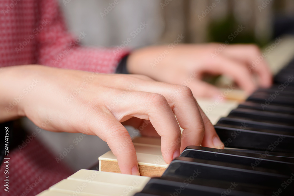 Fototapeta premium Close up photo of hands of a small talented girl playing the piano at home, performing classical music at home, getting ready to the cllasses in the music school
