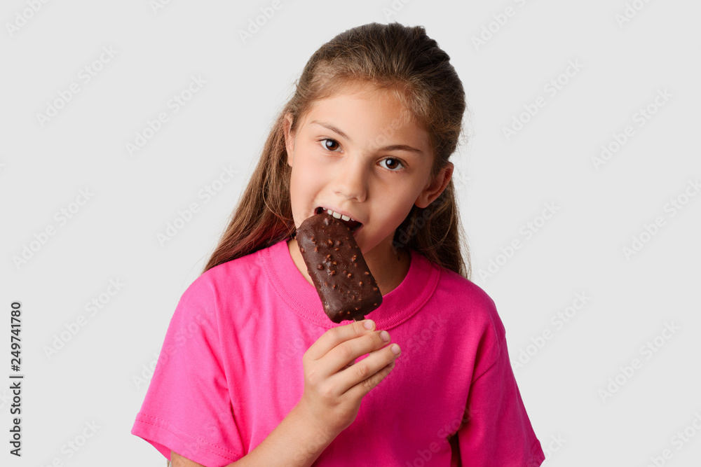 Beautiful girl in a pink T-shirt eating chocolate ice cream with nuts. Small child happy to get tasty ice cream in a hot Summer day Beautiful girl in a pink T-shirt eating chocolate ice cream with nuts. Small child happy to get tasty ice cream in a hot Summer day