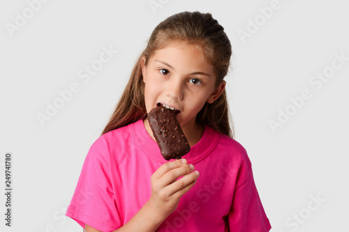 Beautiful girl in a pink T-shirt eating chocolate ice cream with nuts. Small child happy to get tasty ice cream in a hot Summer day
