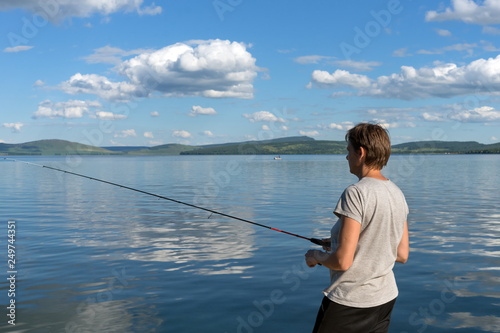 A woman fisherman catches fish for a bait from a blue lake on the background of a mountainous coast. Bright shot.