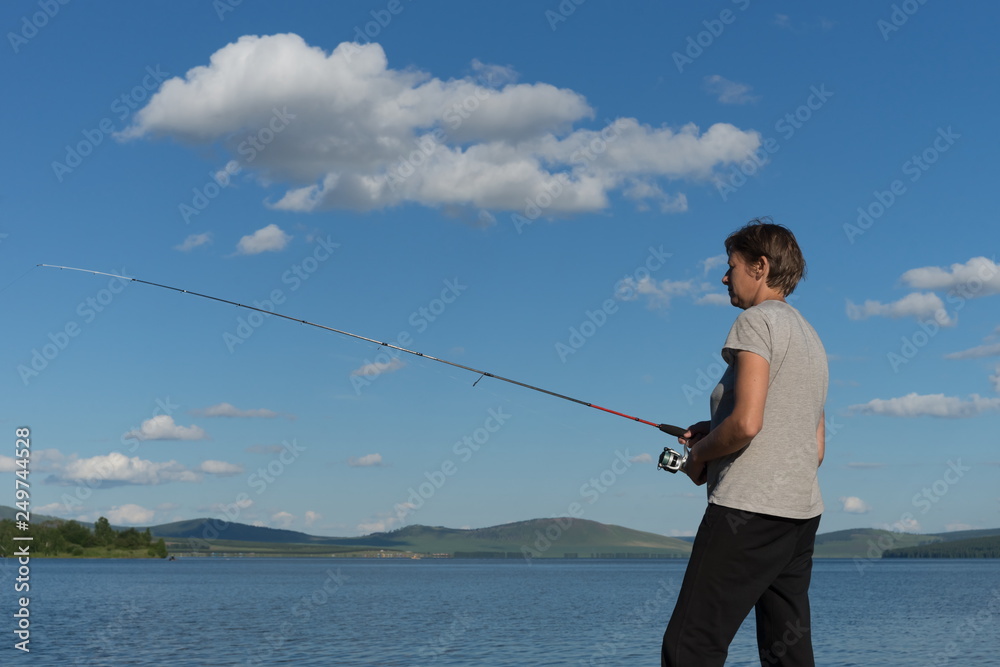 Woman fisherman catches a fish from a blue lake against a blue sky with clouds. Natural shot. Woman fisherman catches a fish from a blue lake against a blue sky with clouds. Natural shot.